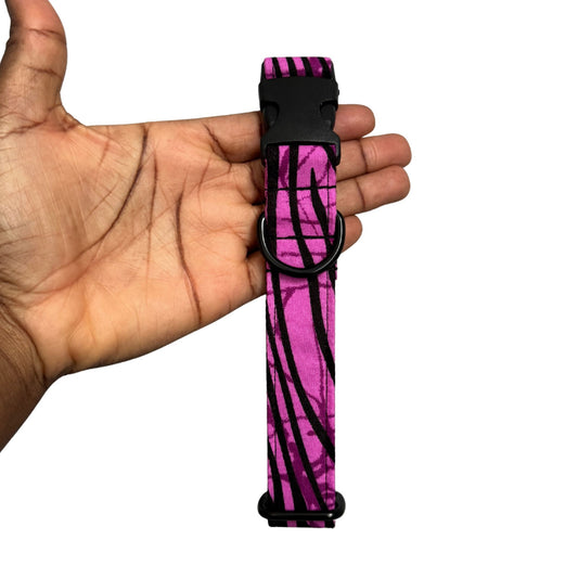 Pink and black zebra patterned dog collar held in a hand against a white background