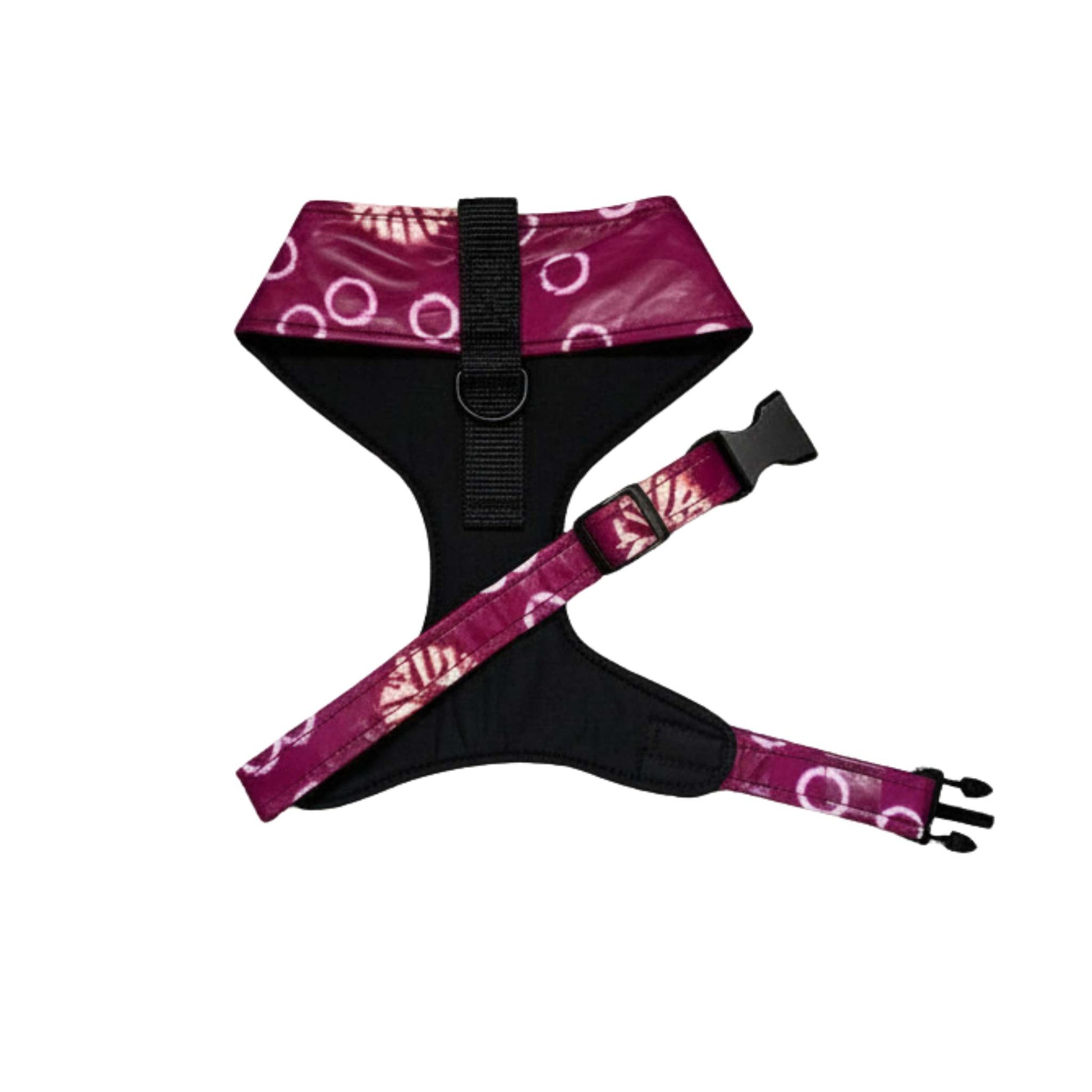 A dog harness with a black padded body and magenta-purple patterned straps featuring white circular and leaf-like motifs, shown on a plain white background.