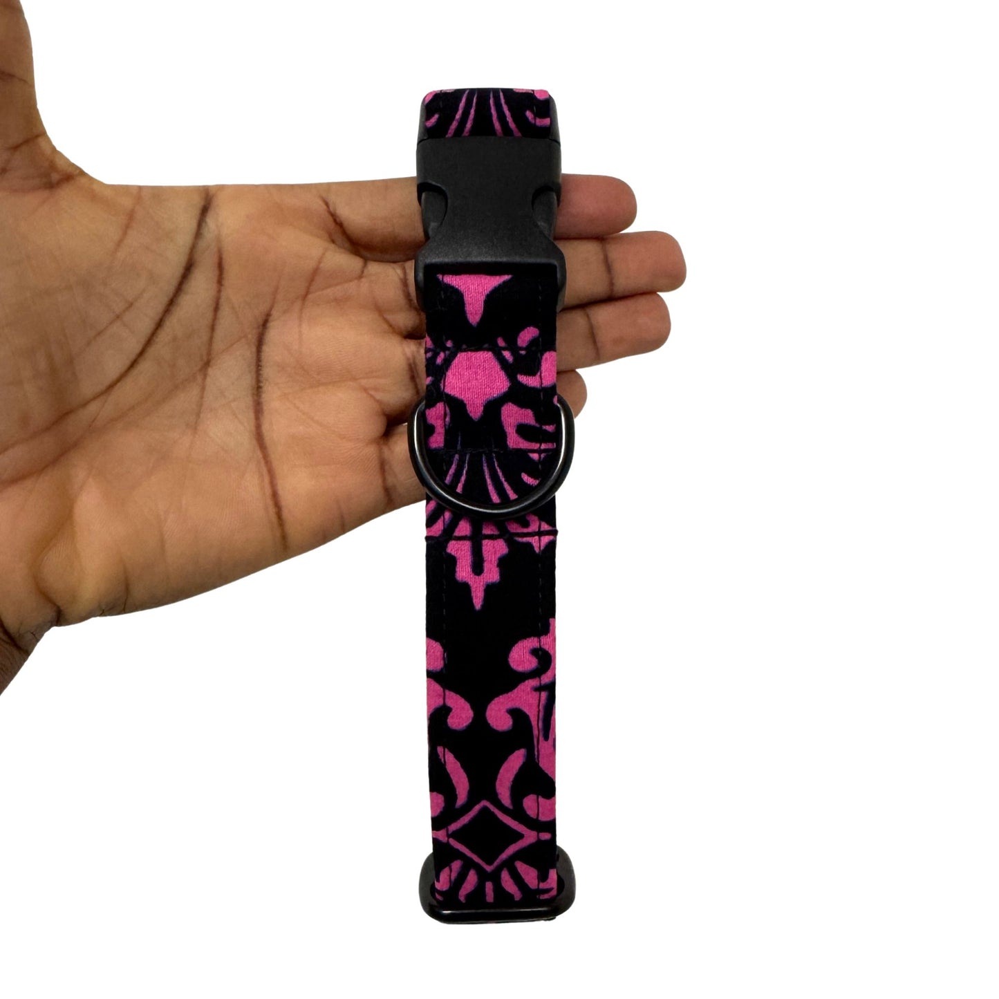 Black and pink patterned dog collar held in a hand against a white background