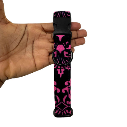 Black and pink patterned dog collar held in a hand against a white background