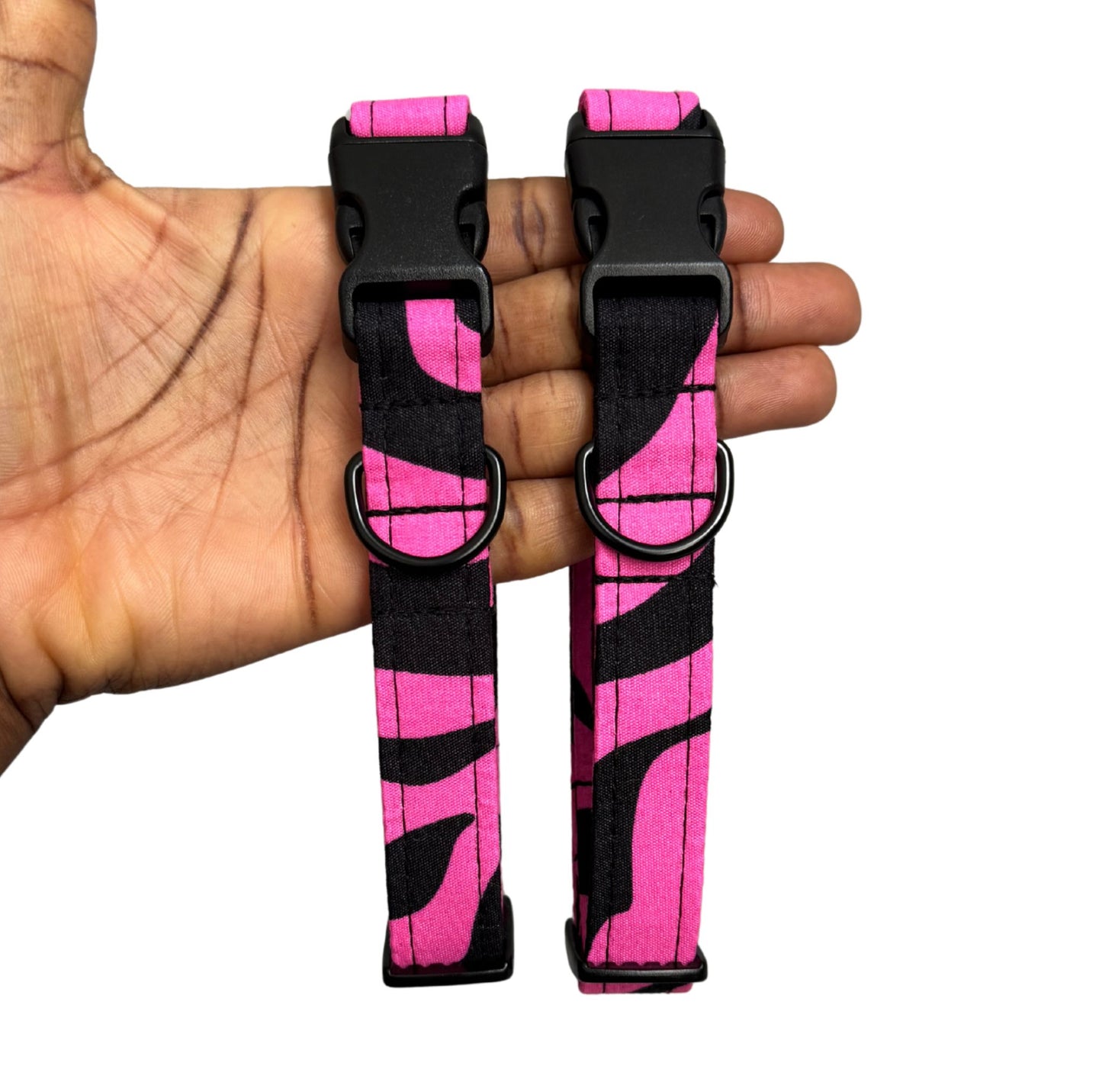 Pink and black striped dog collars held in a hand against a white background