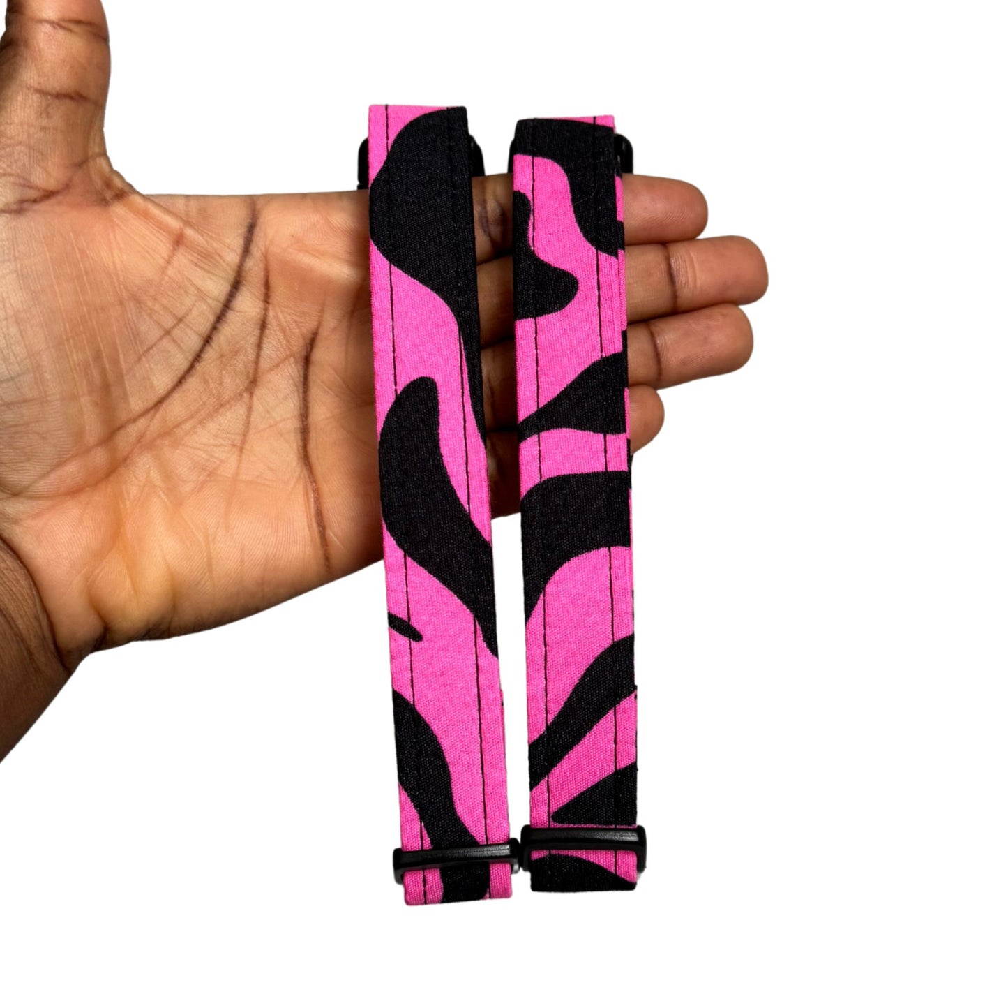 Pink and black zebra patterned straps held in a hand against a white background