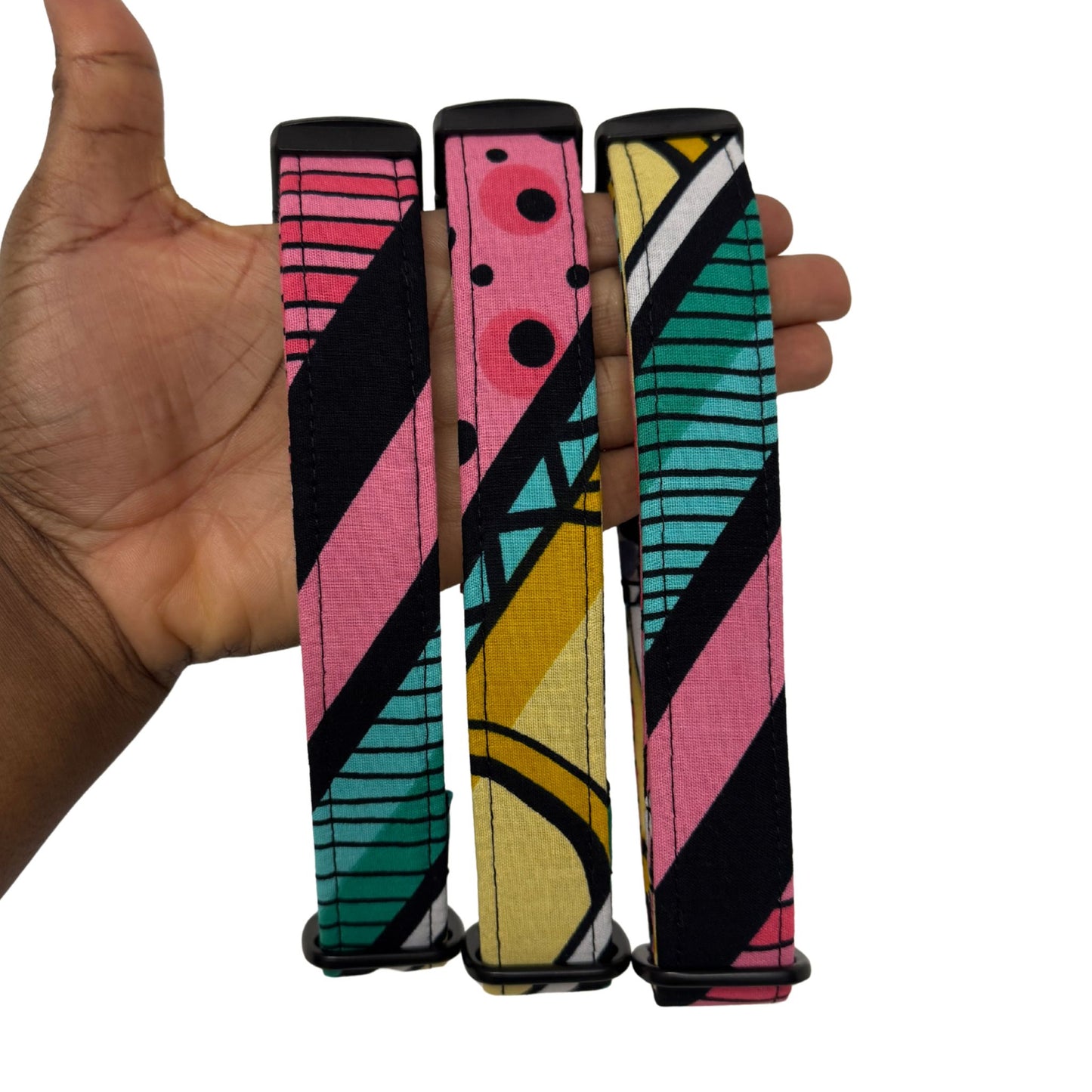 Colorful patterned dog collars held by a hand on a white background